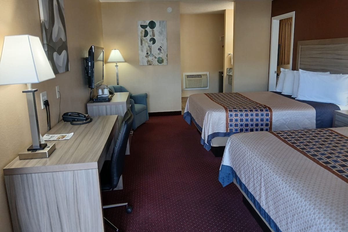 A hotel room with two beds, a desk, a chair, a lamp, and a painting on the wall.