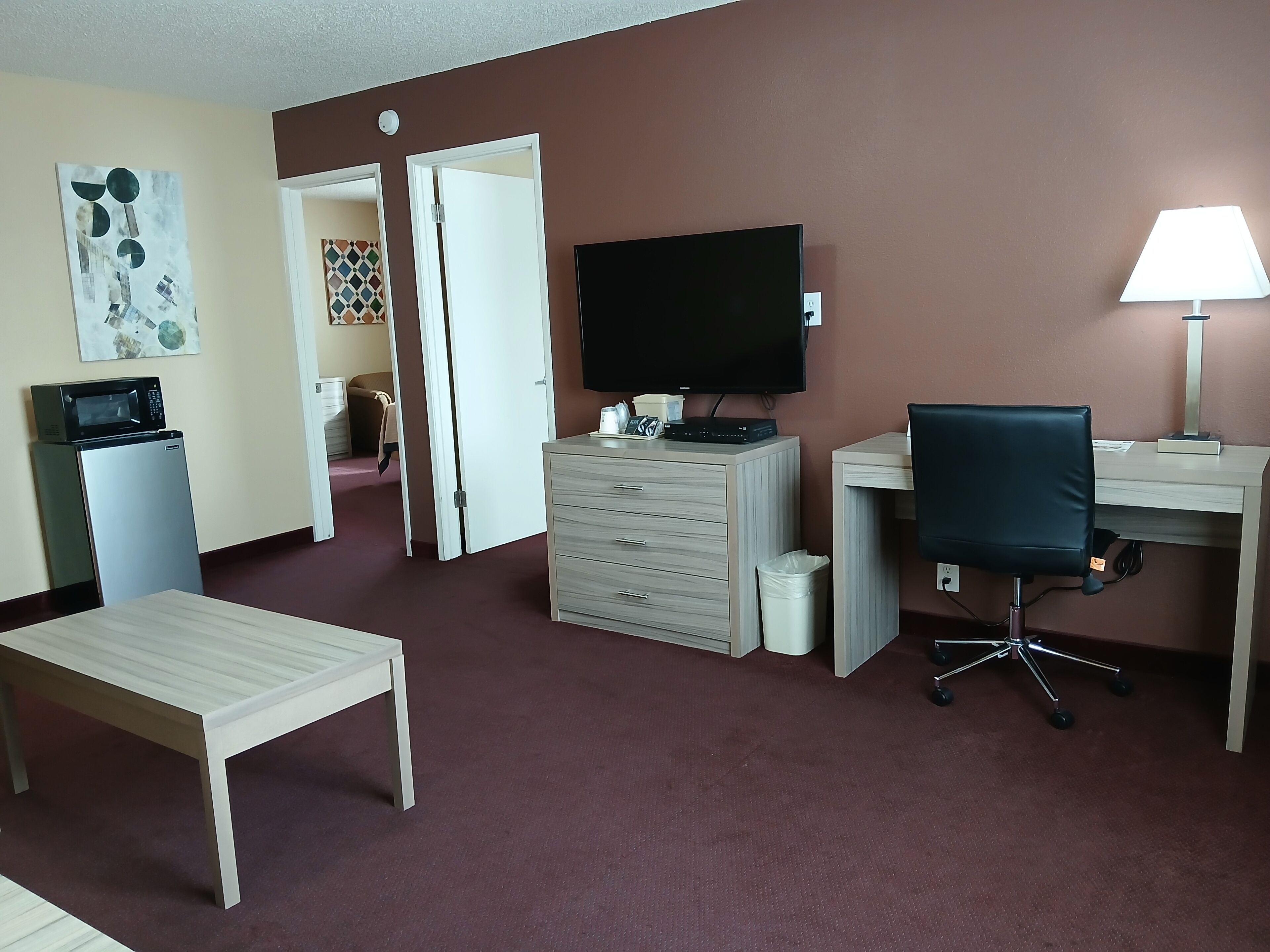 A hotel room with a desk, chair, TV, microwave, and a small table.