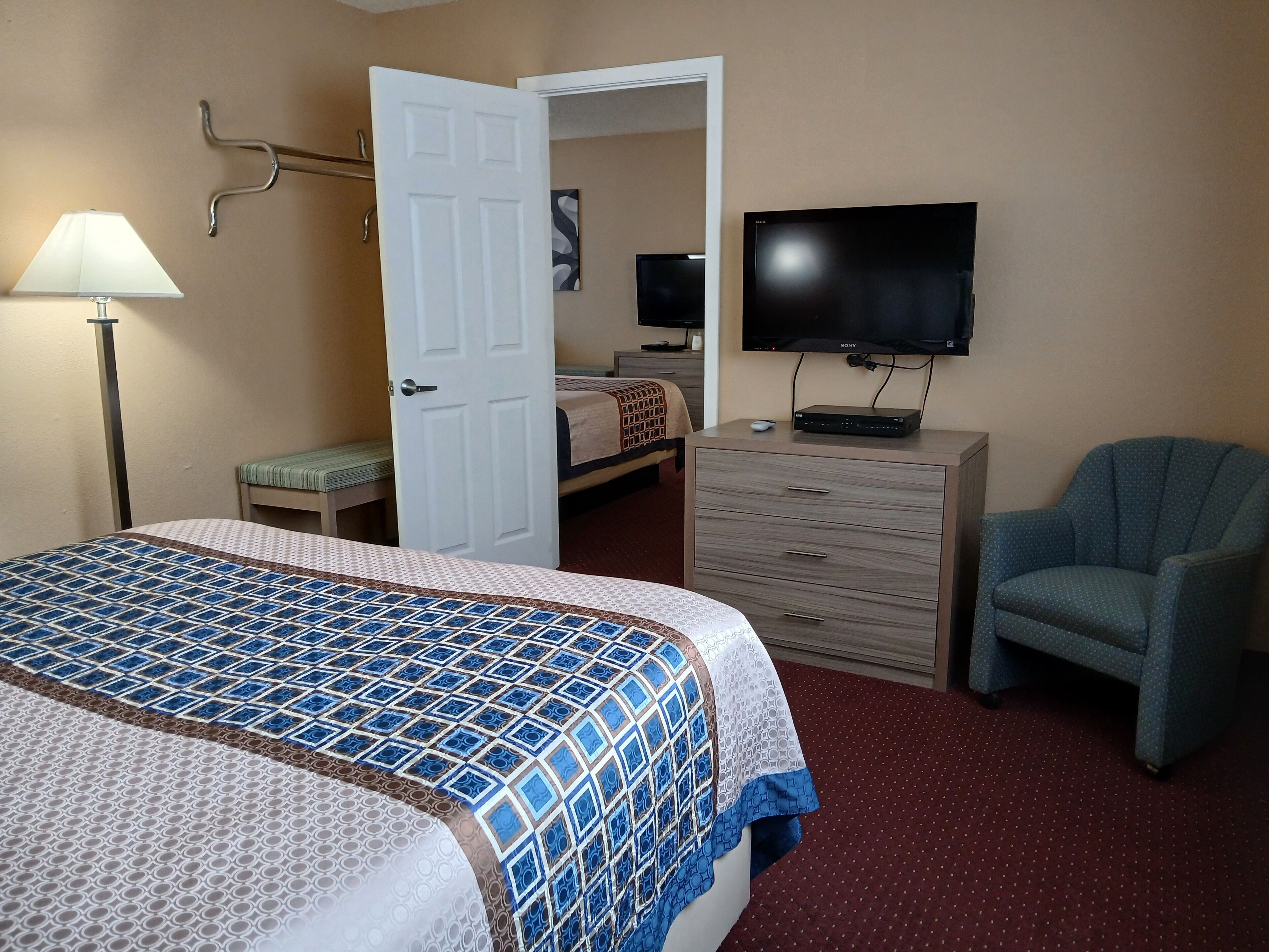 Una habitación de hotel con cama, televisor, silla, cómoda y lámpara.