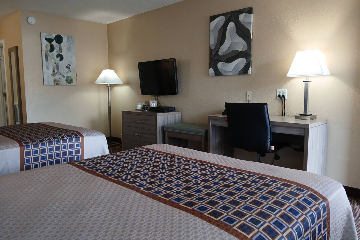A hotel room with two beds, a desk, a chair, a television, and two lamps.