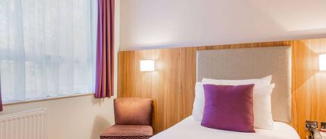 Una habitación de hotel con una cama grande, cabecera de madera, mesita de noche con teléfono y ventana con cortinas traslúcidas.