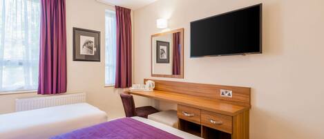 A hotel room with two beds, a desk with a chair, a TV, and framed pictures on the wall.