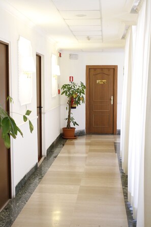 Pasillo de hotel con una puerta de madera que dice 'DIRECTIONS', una planta en maceta y piso de mármol.