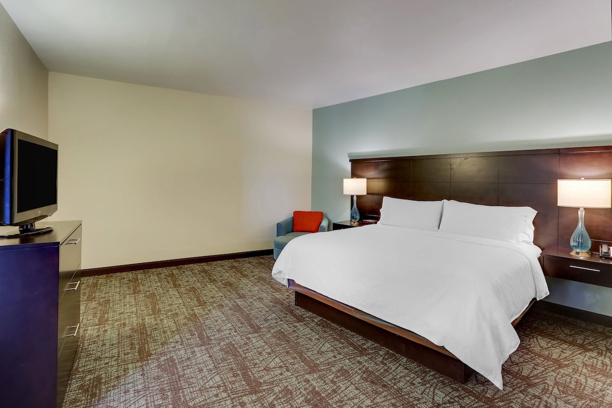 A hotel room with a large bed, a TV on a dresser, a chair, and two bedside lamps.
