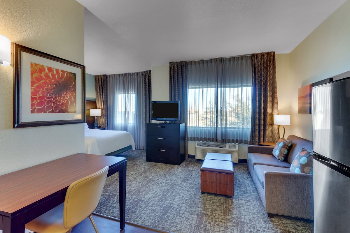 A hotel room with a bed, a desk, a sofa, a TV, and a refrigerator.