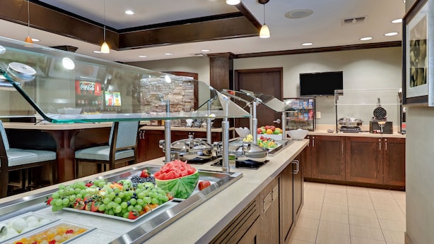 A buffet area with various food options, a Coca-Cola refrigerator, and a stone wall. - Staybridge Suites San Angelo by IHG (San Angelo)