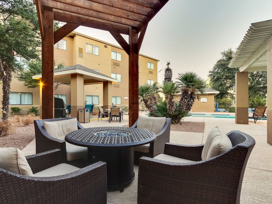 Un espacio al aire libre con patio, mobiliario de mimbre, una mesa redonda y una estructura de pérgola.