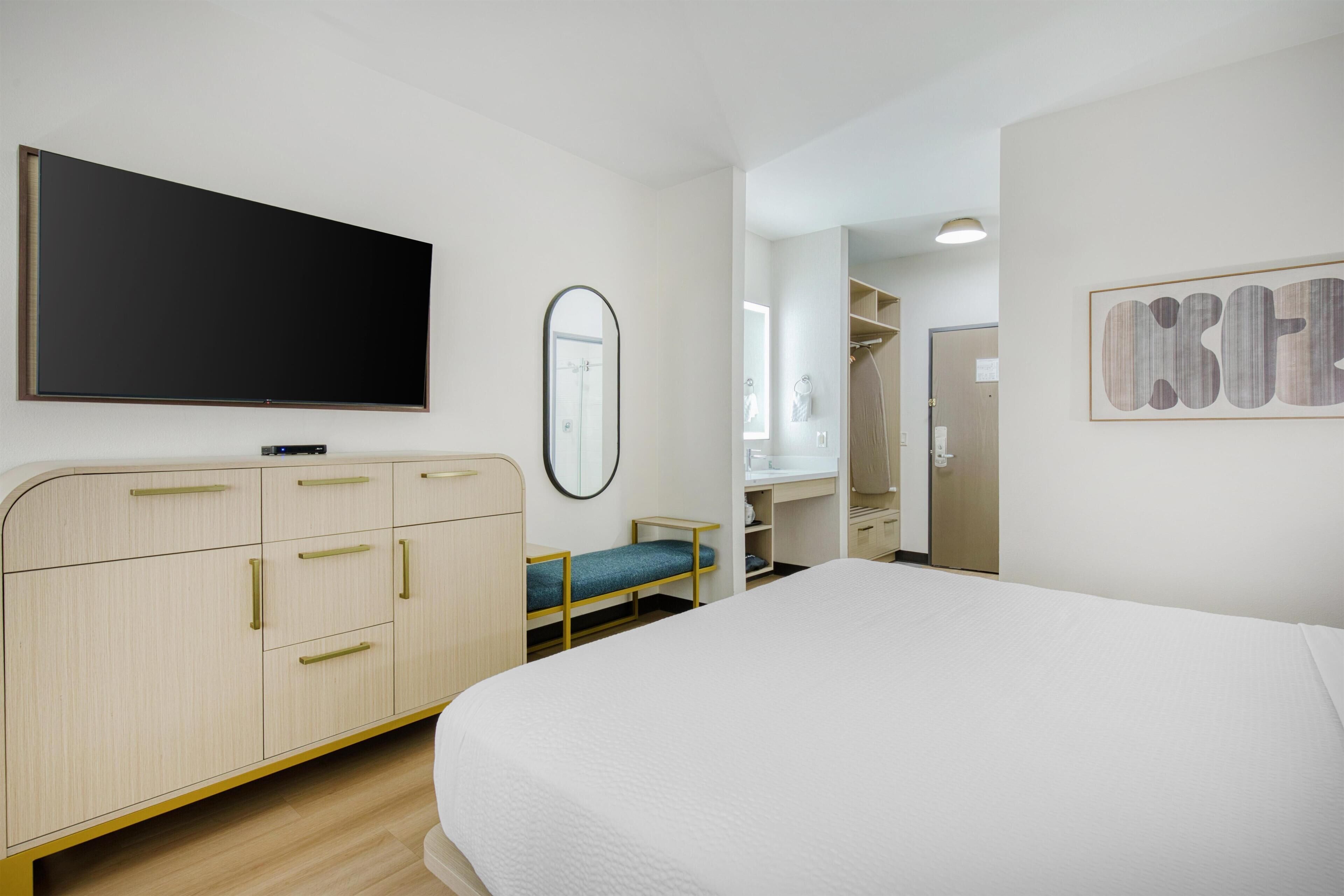 A hotel room with a bed, a TV, a mirror, and a wardrobe.