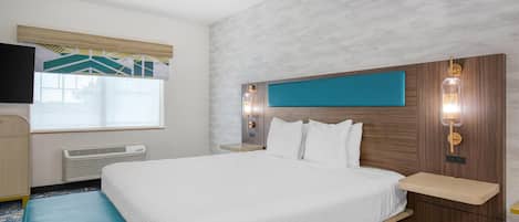 A hotel room with a bed, a bench, a TV, a window, and a wall-mounted light fixture.