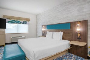 A hotel room with a bed, a bench, a TV, a window, and a wall-mounted light fixture. - Best Western Northwest Lodge (Boise)