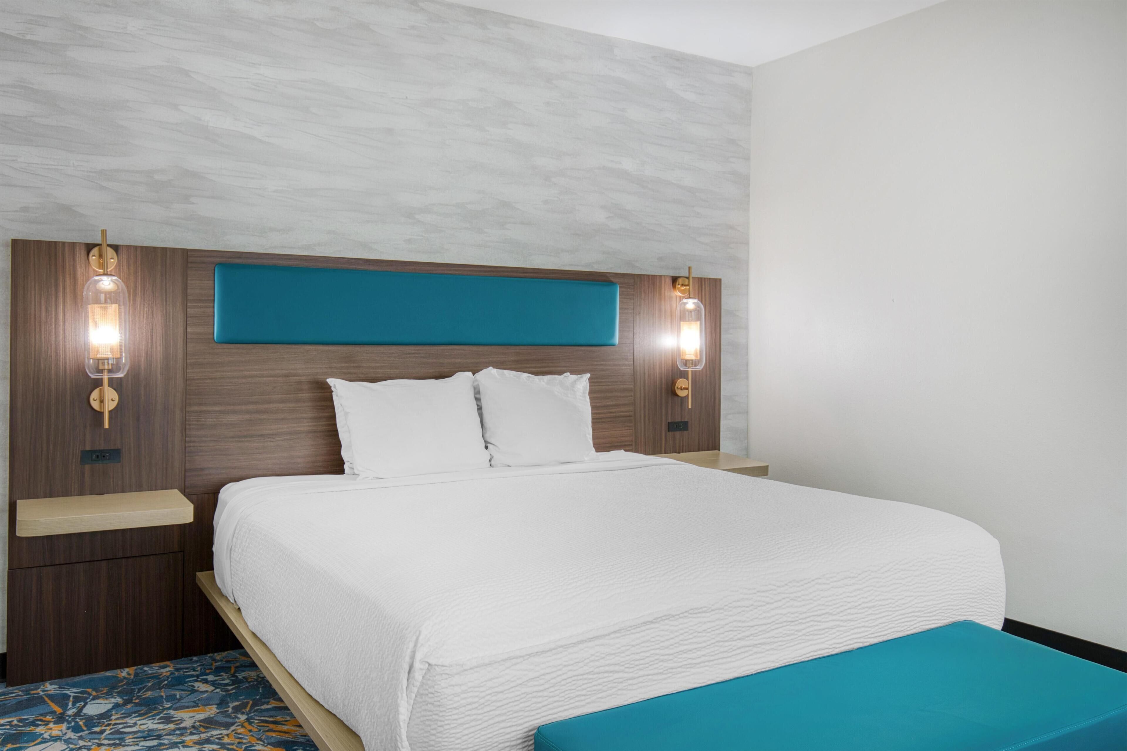 A hotel room with a bed, two bedside tables, a headboard with built-in lighting, and a patterned carpet.