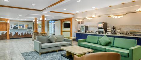 A hotel lobby with a reception desk, seating area with sofas, a coffee bar, and a television screen.