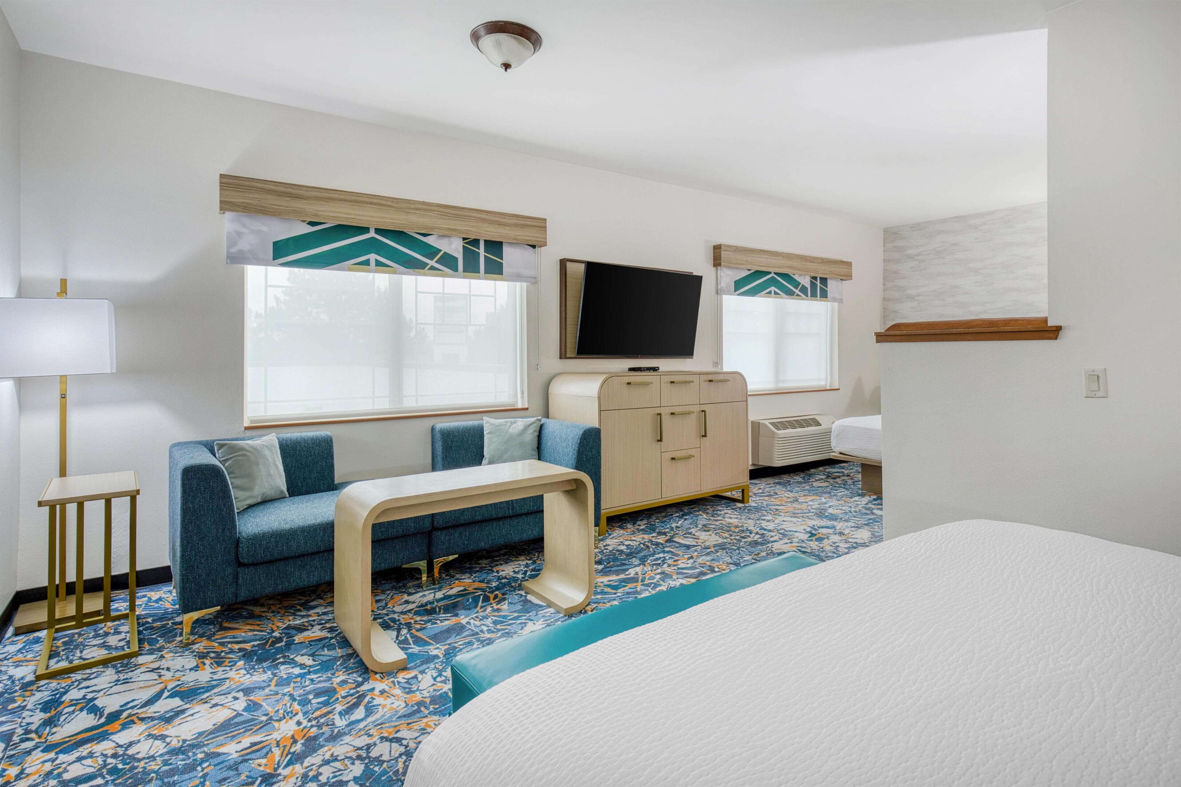 Une chambre d’hôtel avec un lit, un canapé, une télévision, une commode et une petite table.