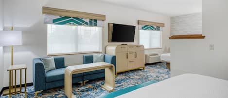 Una habitación de hotel con cama, sofá, televisión, cómoda y una mesita.