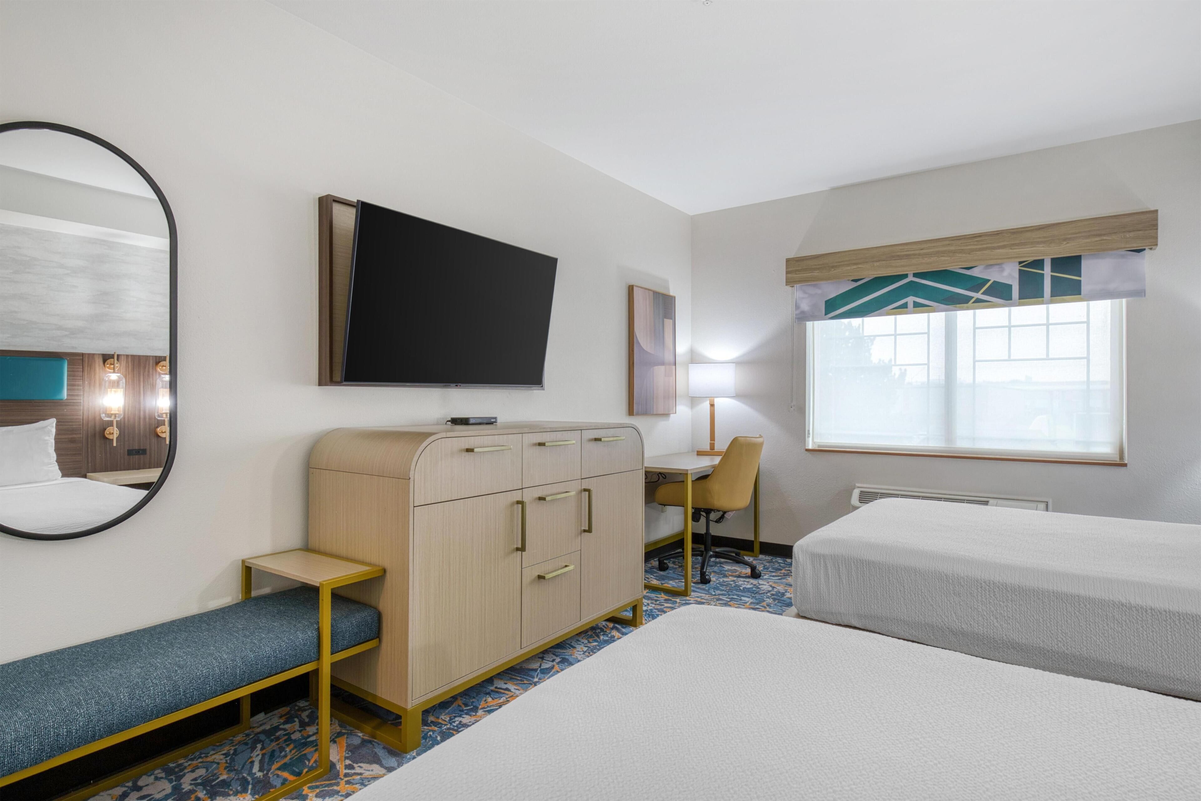 Een hotelkamer met een bed, een bureau, een stoel, een kledingkast, een televisie en een raam met zonwering.
