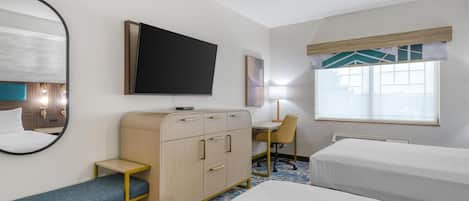 Habitación de hotel con cama, escritorio, silla, armario, televisor y ventana con persianas.