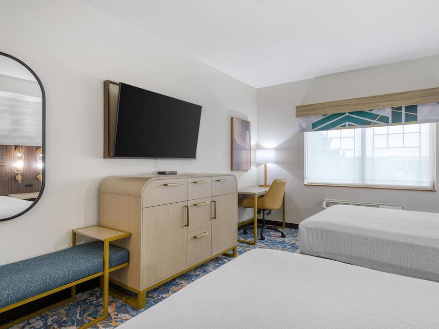 Ein Hotelzimmer mit Bett, Schreibtisch, Stuhl, Kleiderschrank, Fernseher und einem Fenster mit Jalousien.