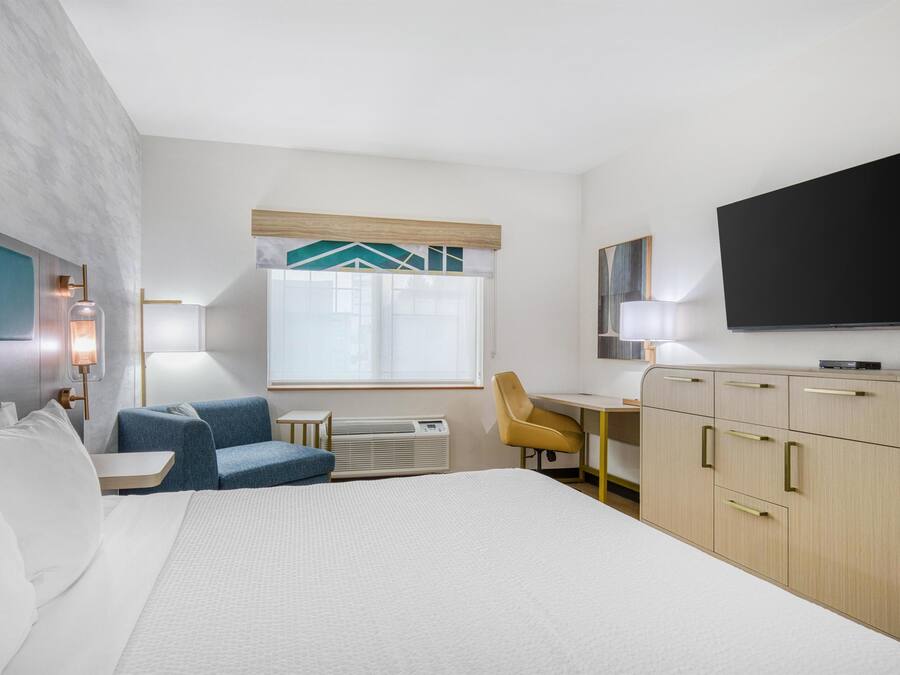 Une chambre d’hôtel avec un lit, un bureau, une chaise, une télévision et une fenêtre avec des rideaux.