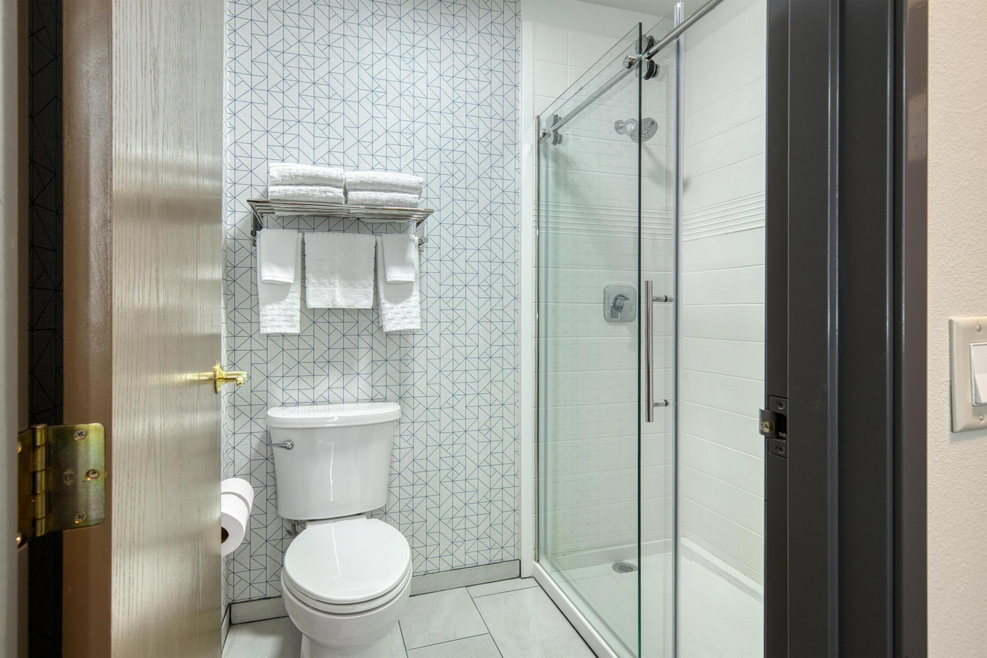 A bathroom with a toilet, a glass shower enclosure, and a towel rack with folded towels.
