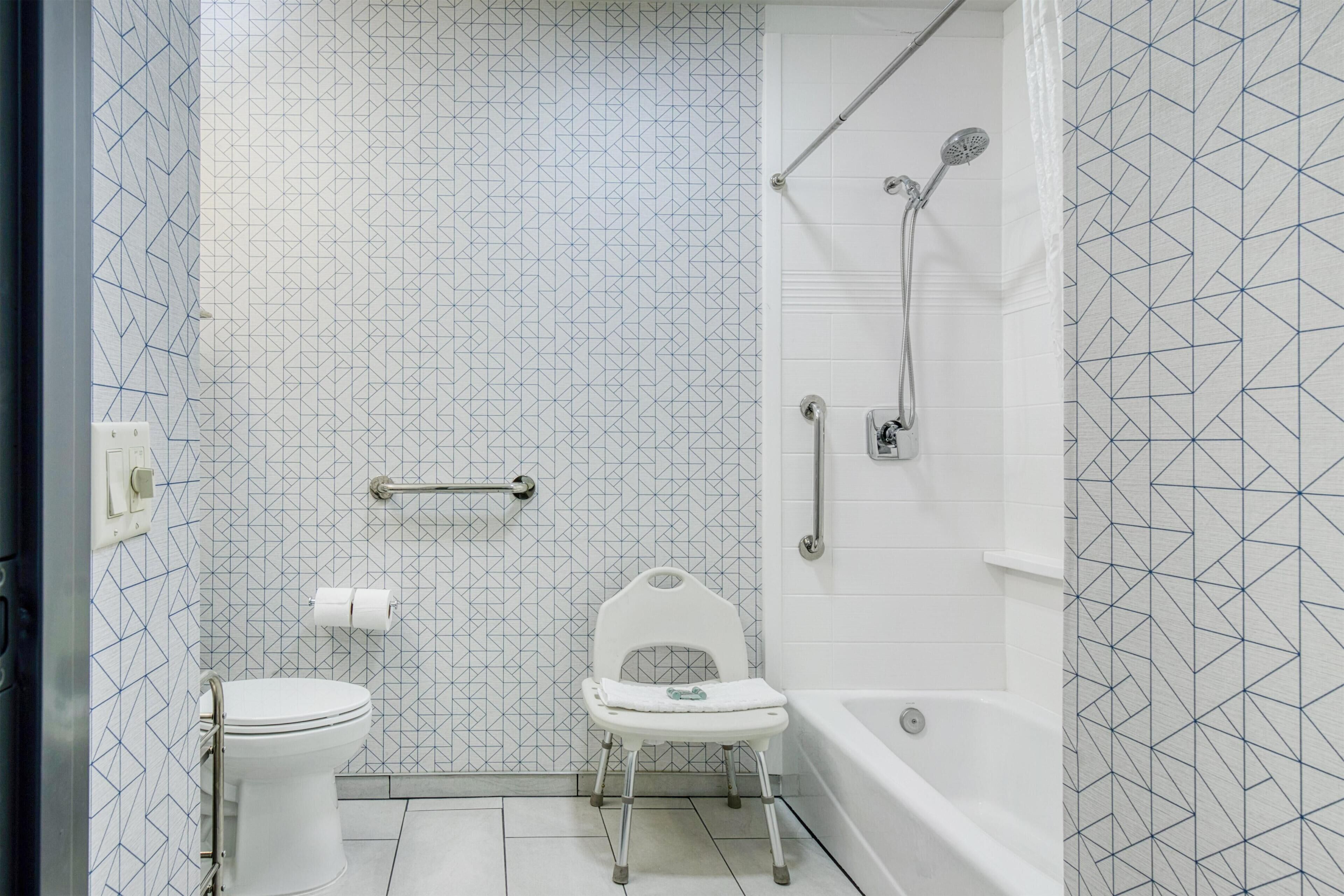 Une salle de bain avec des toilettes, une douche équipée d’un pommeau de douche à main et une chaise blanche.