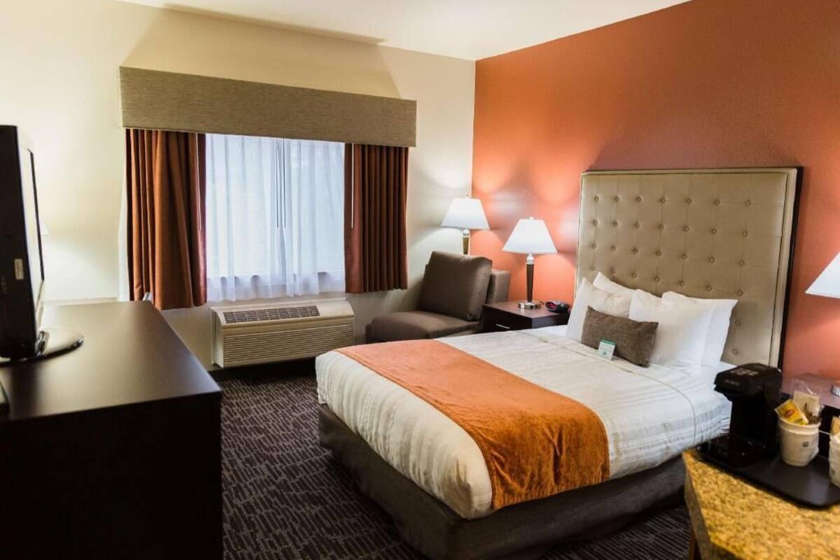 A hotel room with a bed, a desk, a chair, two lamps, and a television.