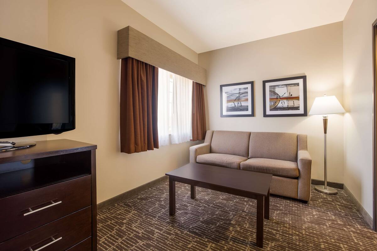 A hotel room with a flat-screen TV, a sofa, a coffee table, a lamp, and two framed pictures on the wall.