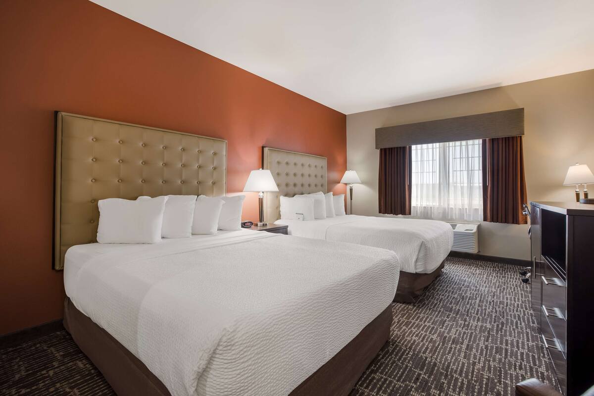 A hotel room with two beds, a TV, and a large window with curtains.