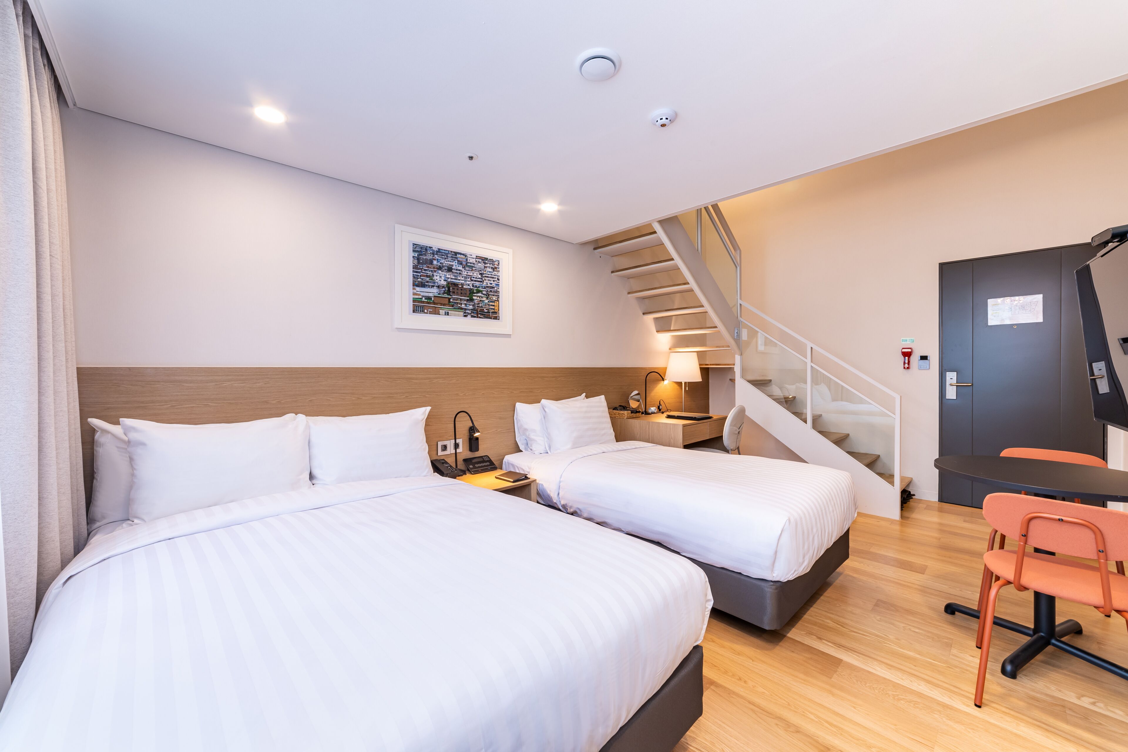 A hotel room with two beds, a desk, a chair, a TV, and a staircase.