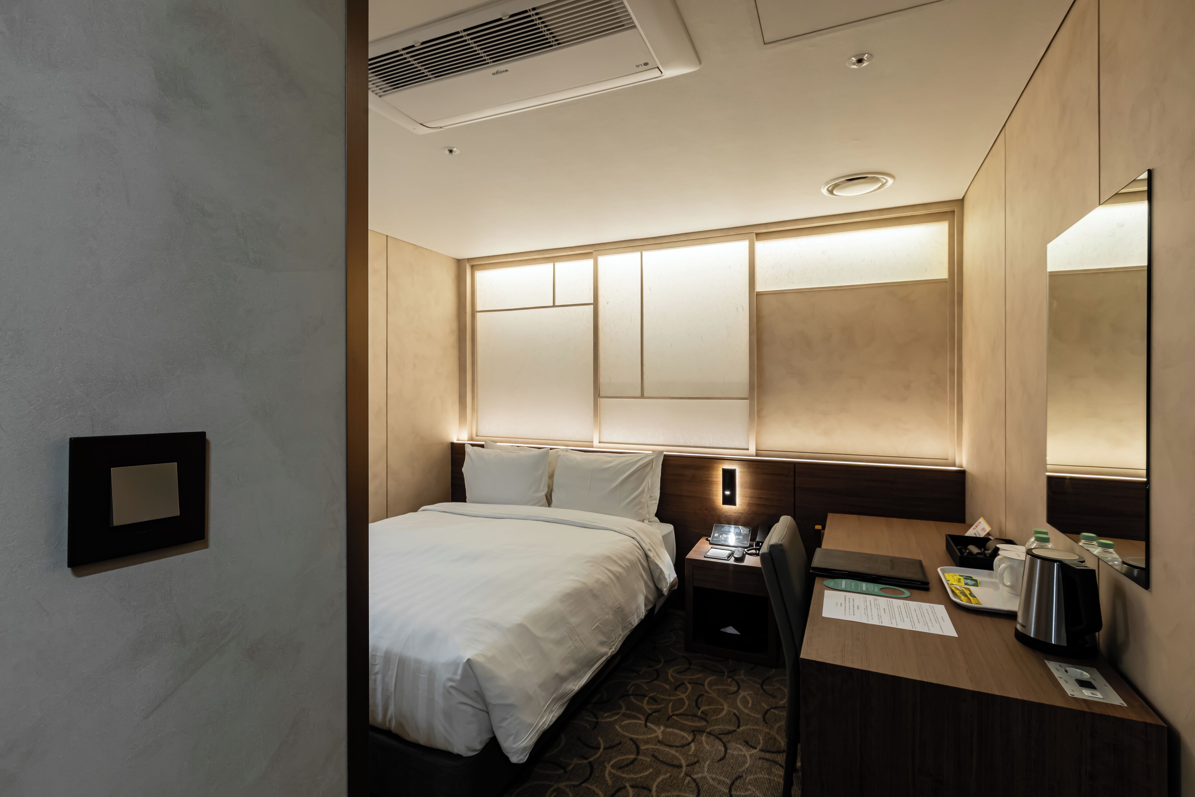Ein Hotelzimmer mit einem großen Bett, einem Schreibtisch mit einem Laptop, einer Kaffeemaschine und einem Spiegel.