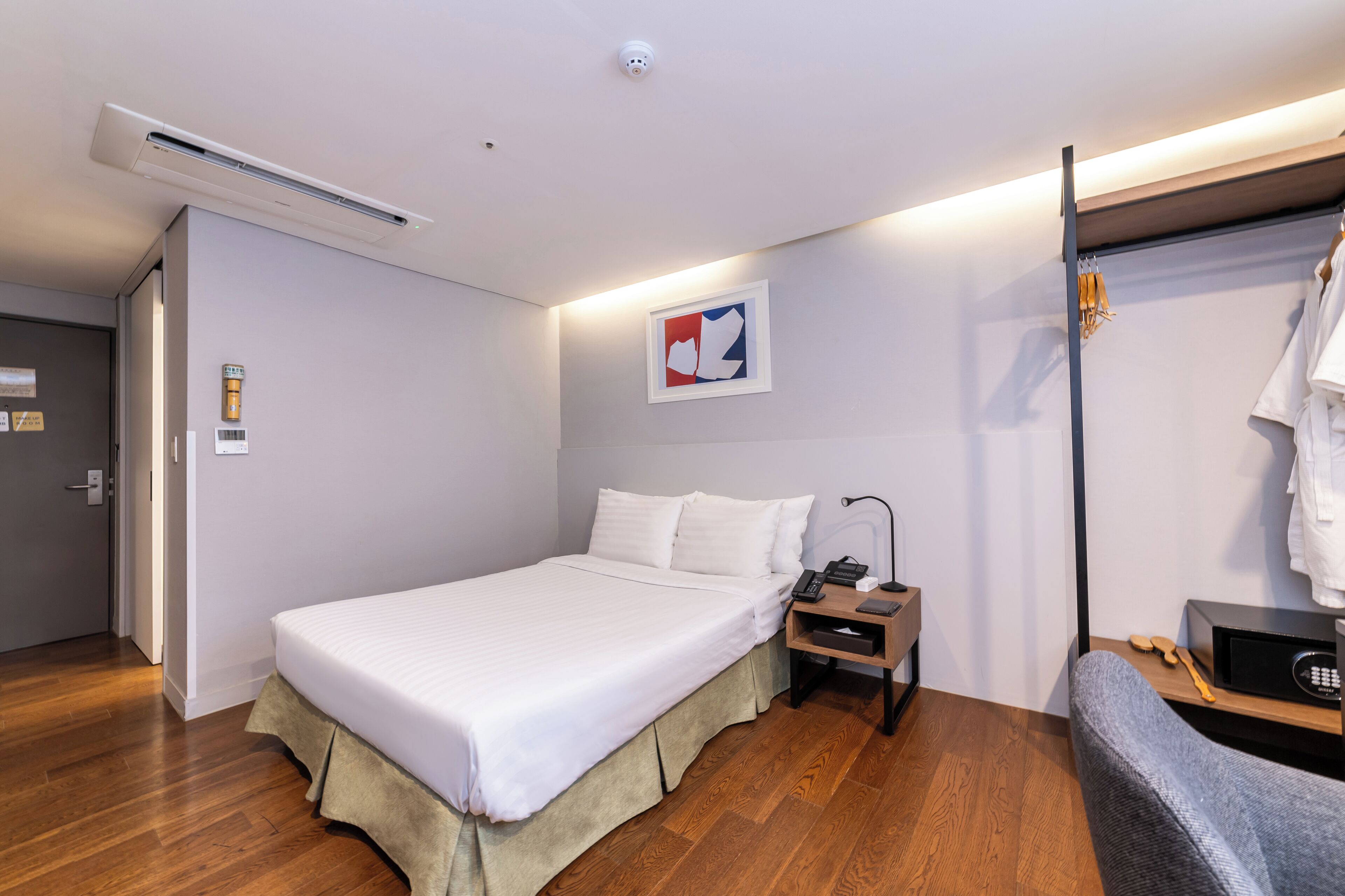Una habitación de hotel ordenada con cama, mesita de noche y un pequeño rincón de descanso.