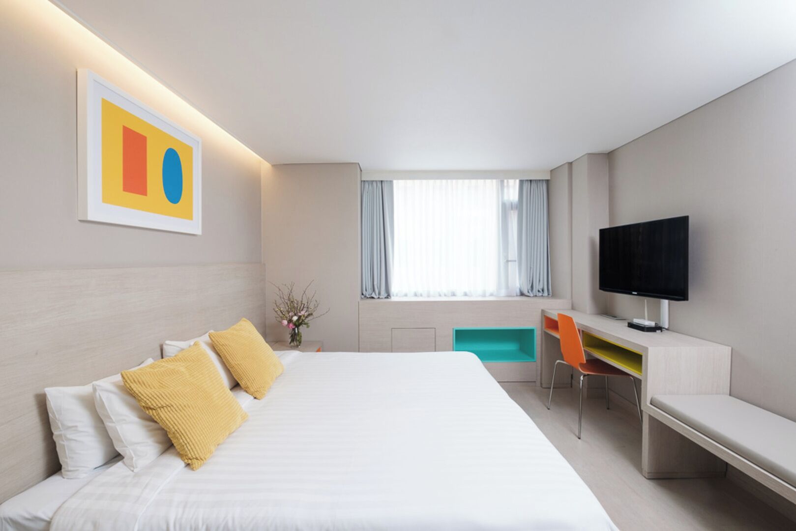 A modern hotel room with a large bed, a desk, a television, and a window with curtains.