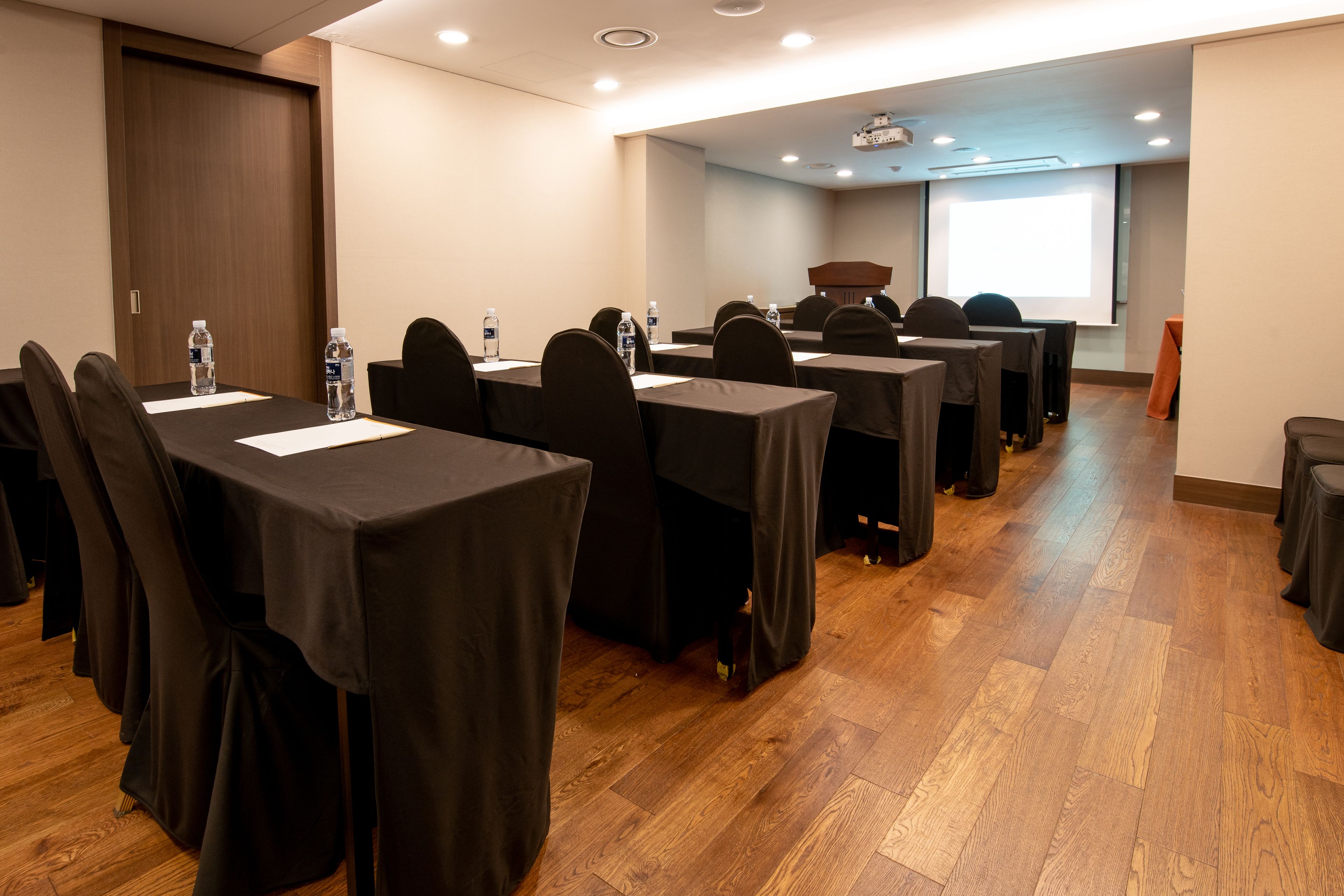 A conference room with multiple tables, chairs, and a projector screen.