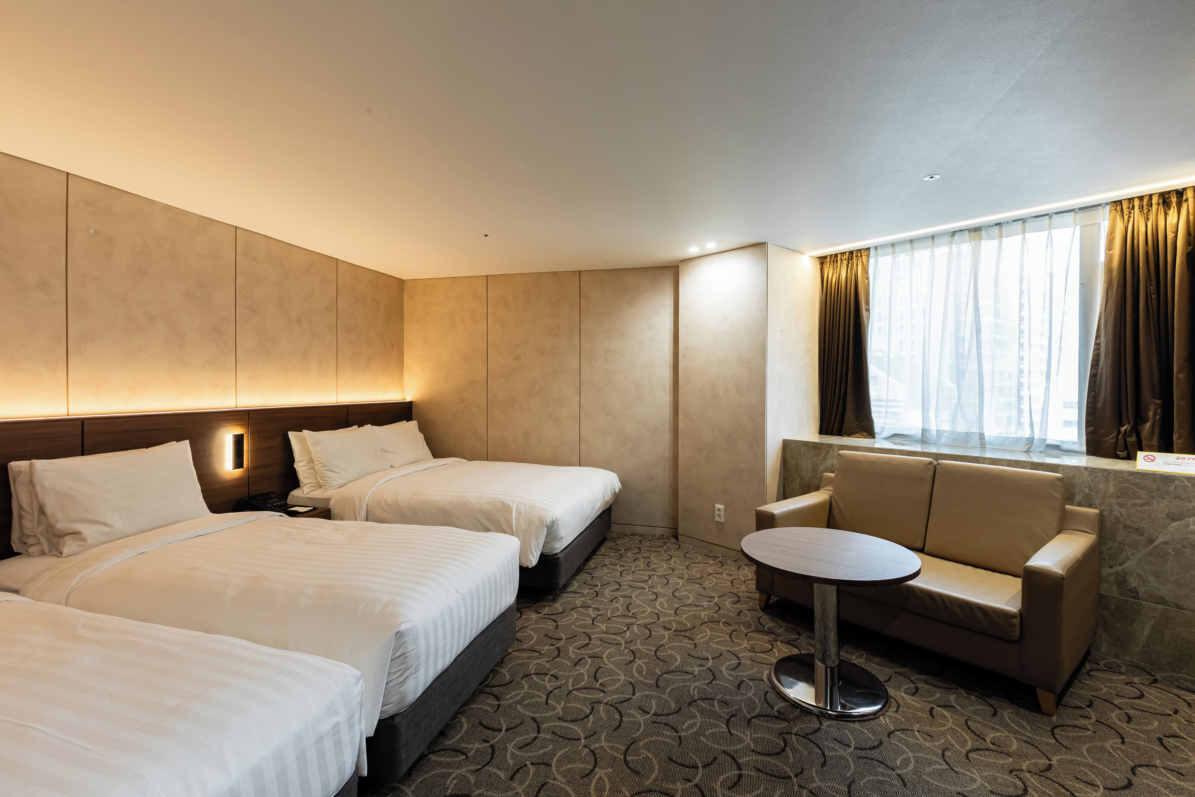 Une chambre d’hôtel avec deux lits, un canapé, une petite table ronde et une fenêtre avec des rideaux.