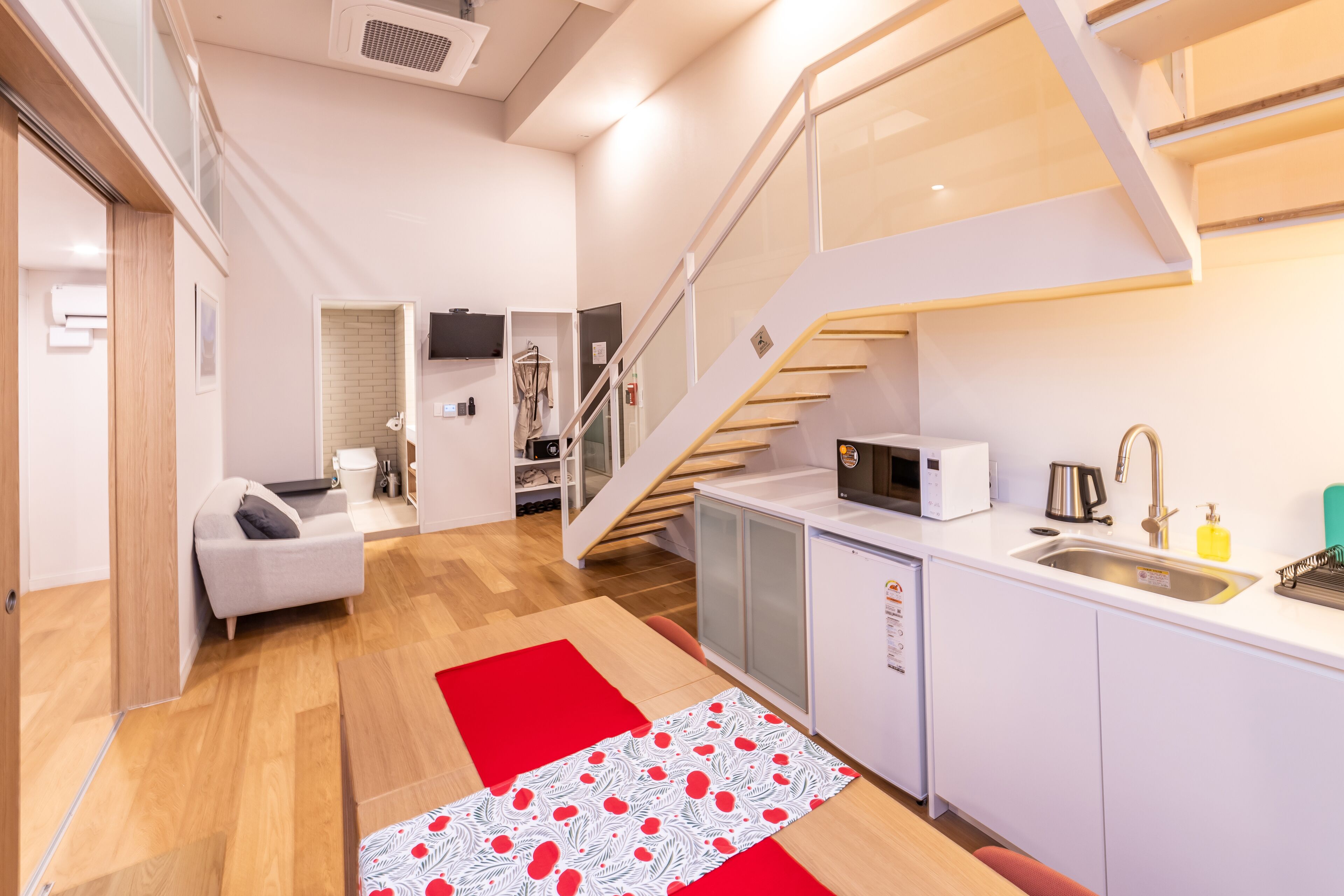 A modern kitchen with a microwave, sink, and cabinets. There is a staircase leading to an upper level.