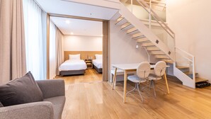 A modern hotel room with a wooden floor, a sofa, a desk with chairs, a bed, and a staircase. - New Seoul Hotel (Seoul)