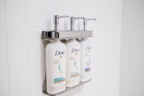 Three Dove shampoo bottles on a white shelf against a white tiled wall. - Holiday Inn Express & Suites Raleigh Durham Airport at RTP by IHG (Durham)