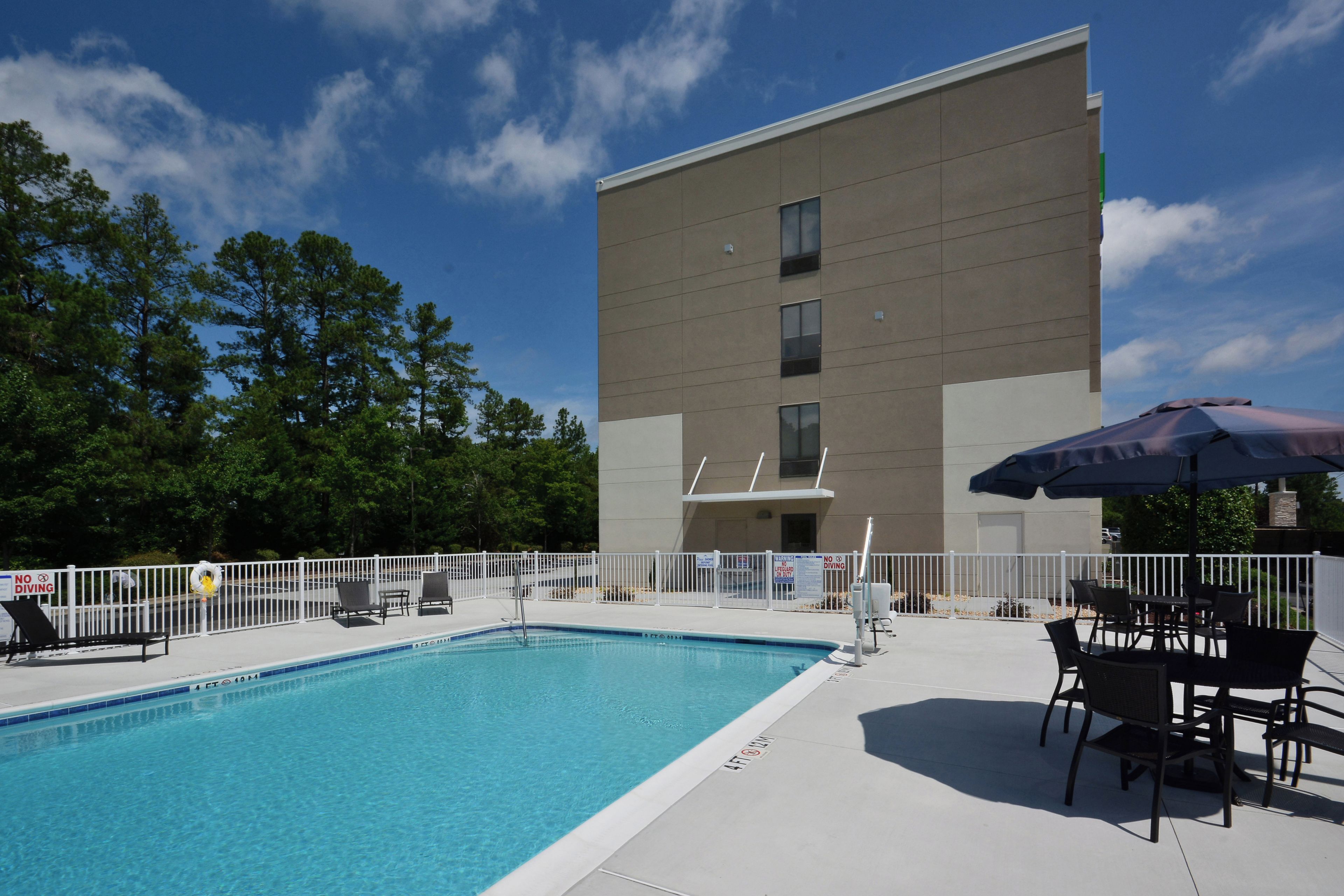 A swimming pool with a white fence, lounge chairs, and an umbrella.