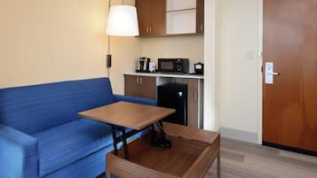 Habitació compacta amb un sofà blau, una taula de fusta petita, un microones, una cafetera i un armari.