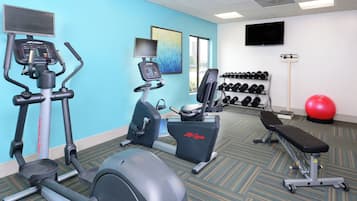 A gym with cardio machines, dumbbells, a bench, and a red exercise ball.
