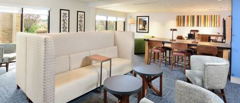 A modern hotel lobby with a sectional sofa, round tables, and a bar area.