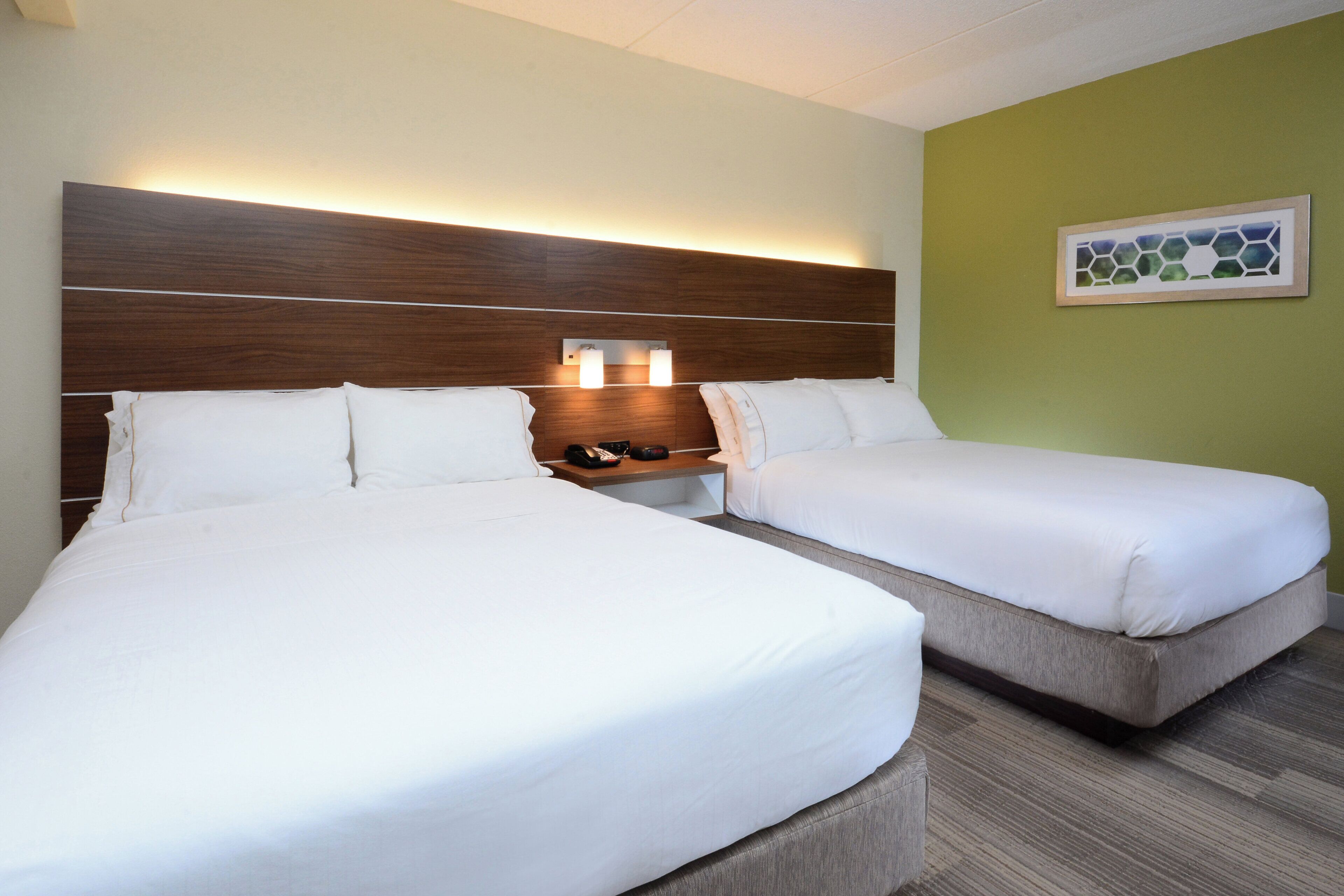 A hotel room with two beds, a wooden headboard, bedside lamps, and a green wall.
