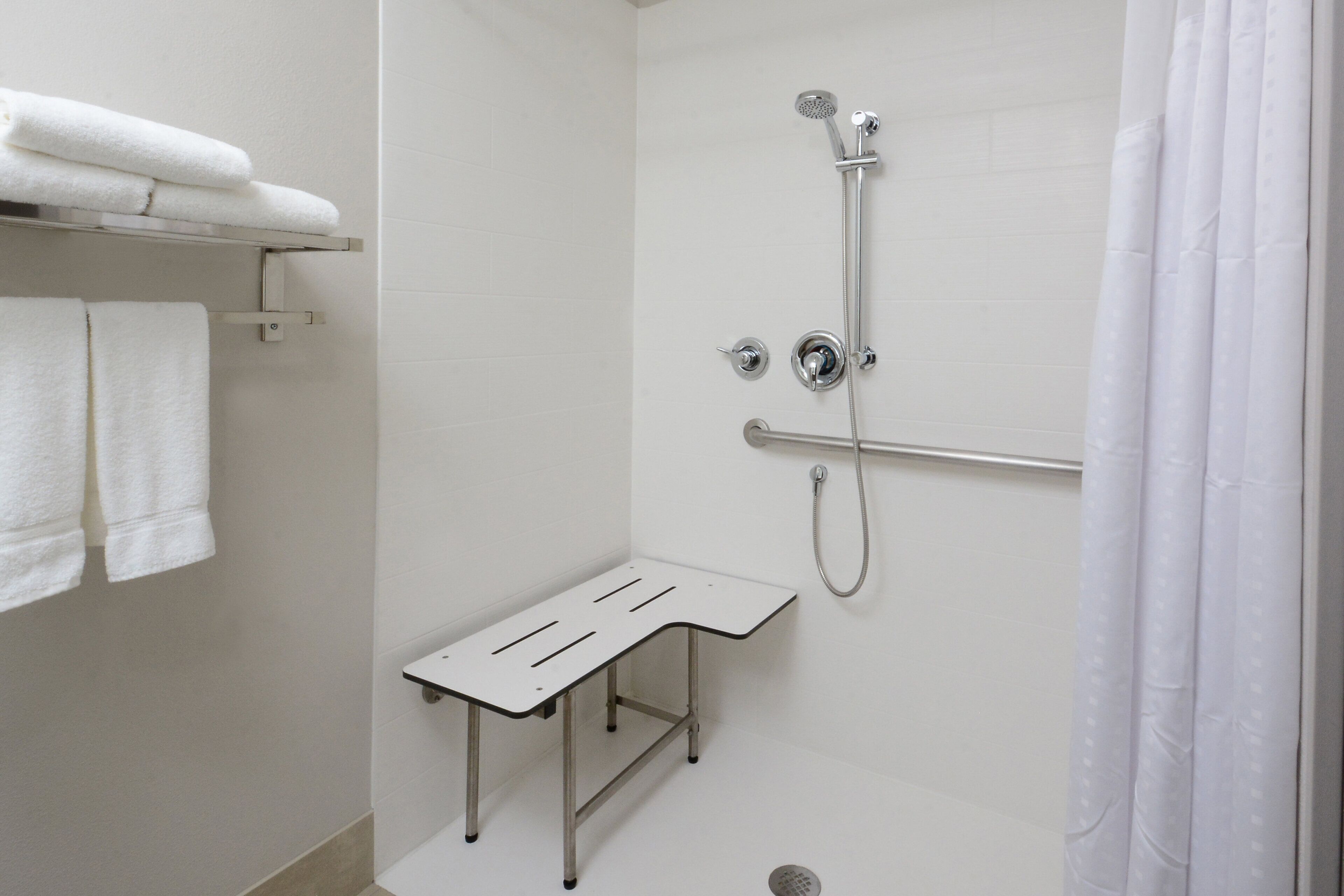 A shower area with a handheld showerhead, a handheld shower attachment, and a shower seat.