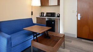 A compact room with a blue sofa, a small wooden table, a microwave, a coffee maker, and a refrigerator. - Holiday Inn Express & Suites Raleigh Durham Airport at RTP by IHG (Durham)