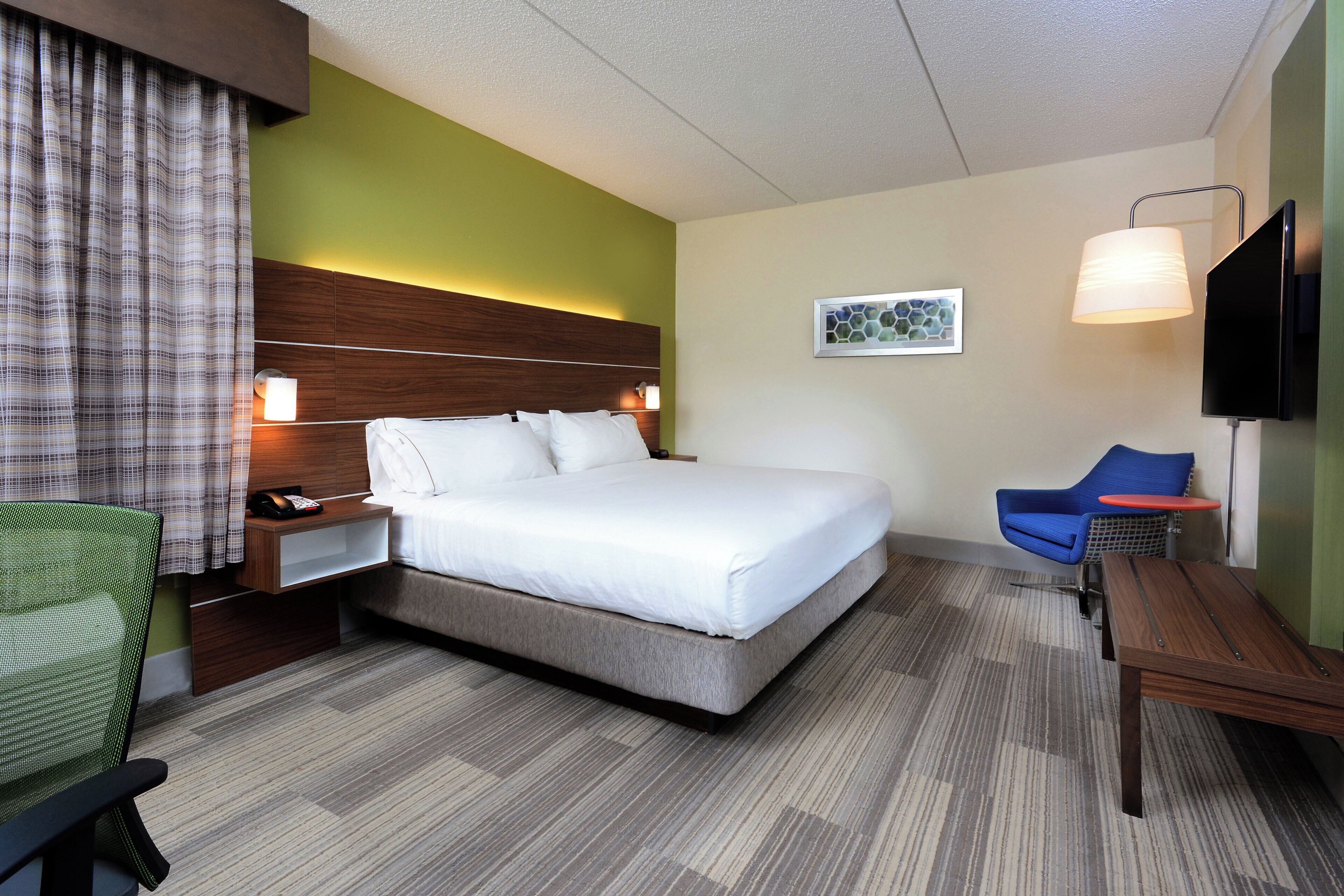 A hotel room with a bed, a desk, a chair, a television, and a painting on the wall.