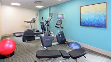 Un gimnasio con máquinas de cardio, una máquina de remo y pelotas de ejercicio.