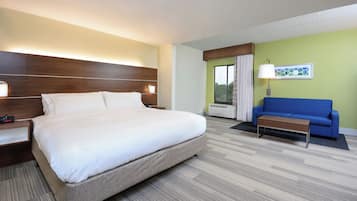 A hotel room with a large bed, a blue sofa, a small table, a nightstand, a lamp, and a window with curtains.