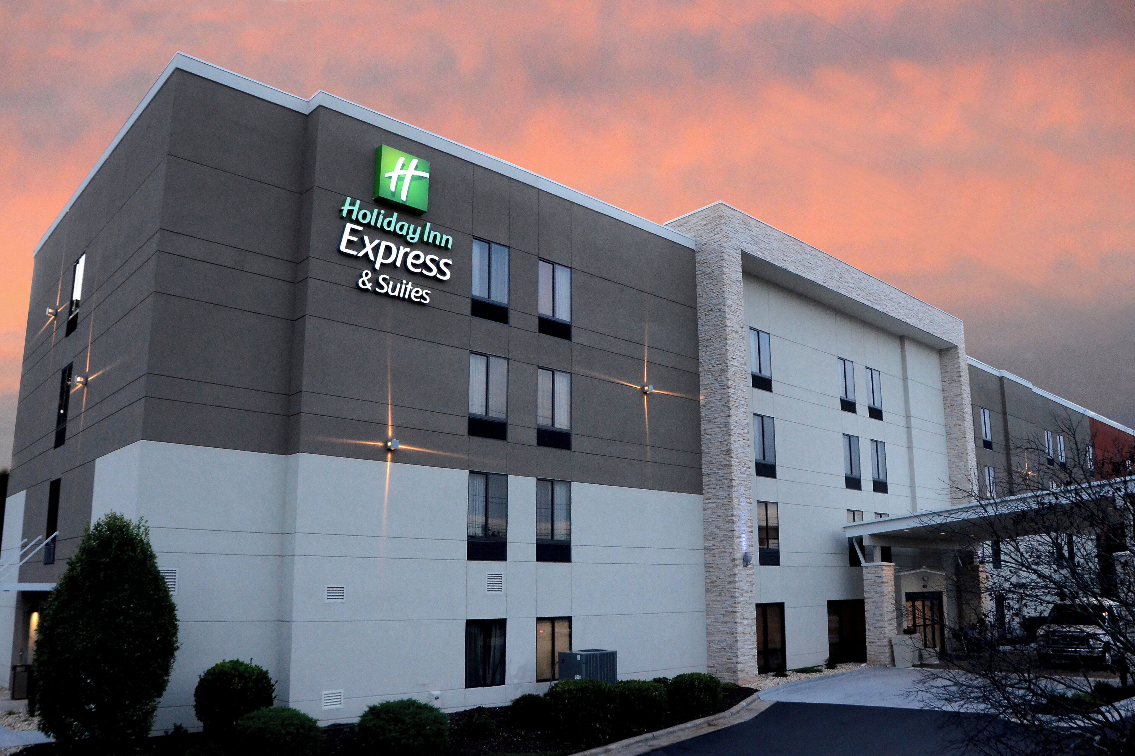 Edificio de un hotel Holiday Inn Express & Suites con diseño moderno, destacando un logo verde y un techo plano.