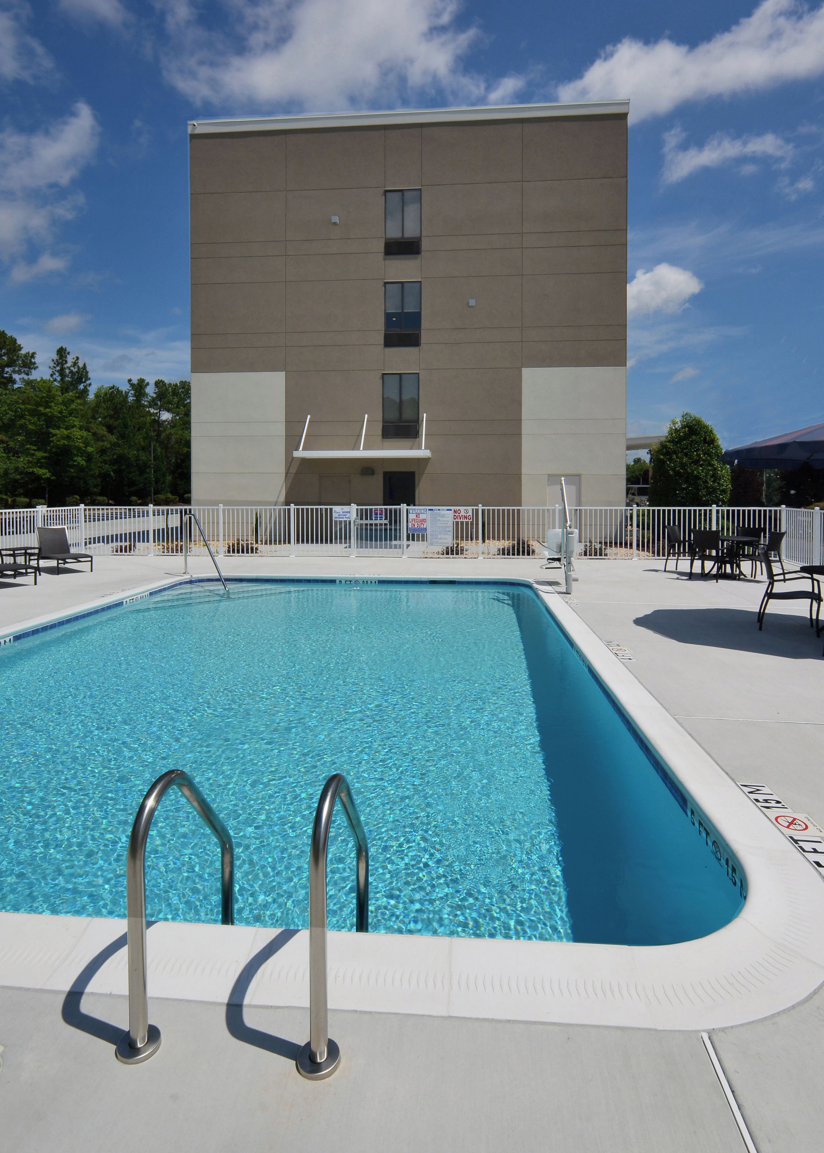 A swimming pool with metal ladders, a white fence, and a building with a flat roof in the background.