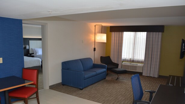 A hotel room with a bed, a blue sofa, a desk with a chair, a small table, and a TV.