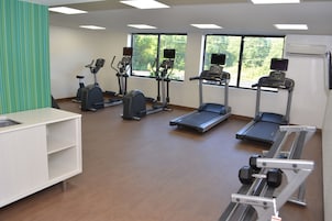 Un gimnasio con cintas de correr, elípticas y una banca para pesas.